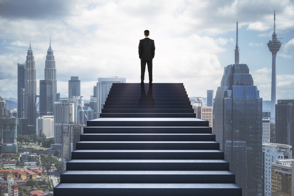 Back view of man standing on stairs on blurry city background. Success and growth concept.
